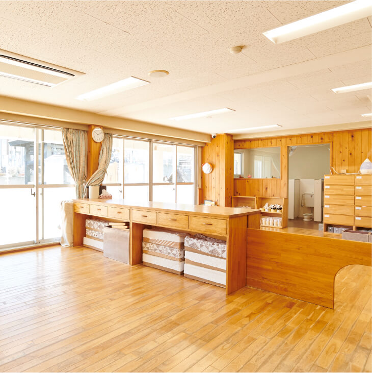 木の温もりが感じられる広々とした保育室。窓際には木製の長い収納棚が置かれ、奥にはトイレが見える。