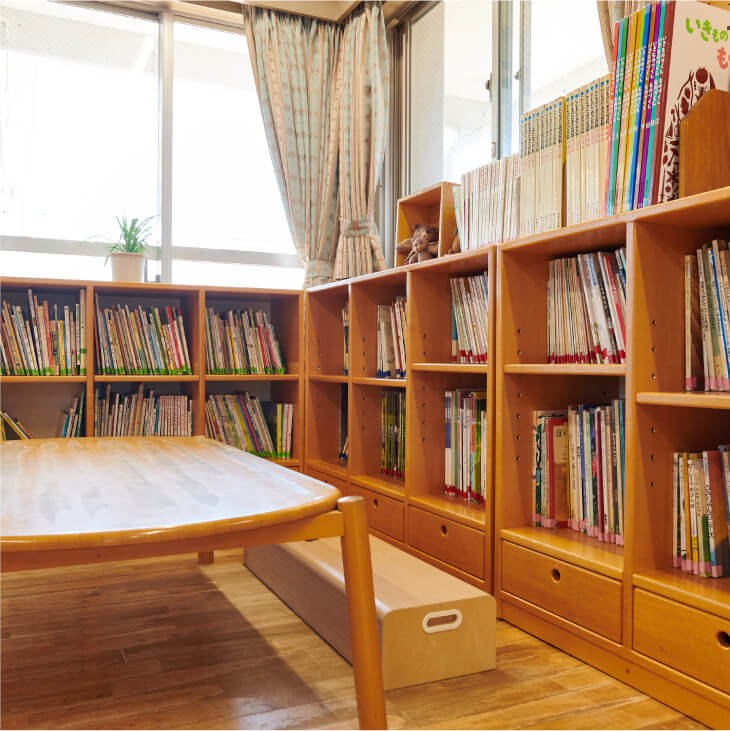 窓際に置かれたL字型の木製本棚に、たくさんの絵本がぎっしりと収納されている図書コーナーのような空間。