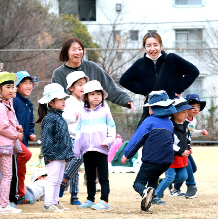 園庭で遊ぶ子どもたちを笑顔で見守る保育士