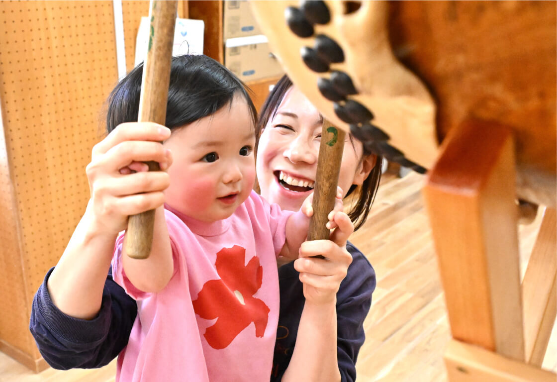 太鼓を叩く子どもを笑顔でサポートする保育士