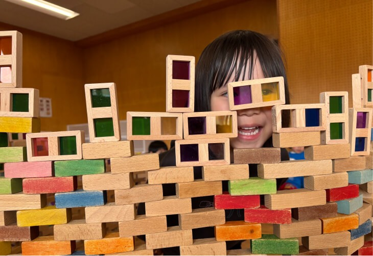 色とりどりの積み木で作った壁の隙間から、笑顔を覗かせる女の子