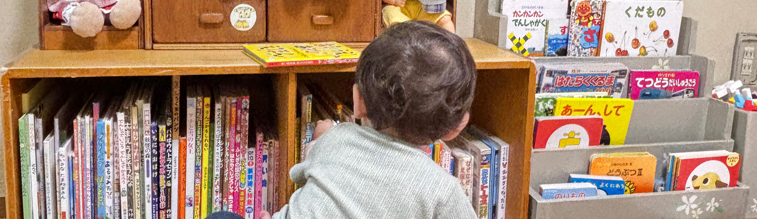 本棚の前で、座りながら本を選ぶ男の子