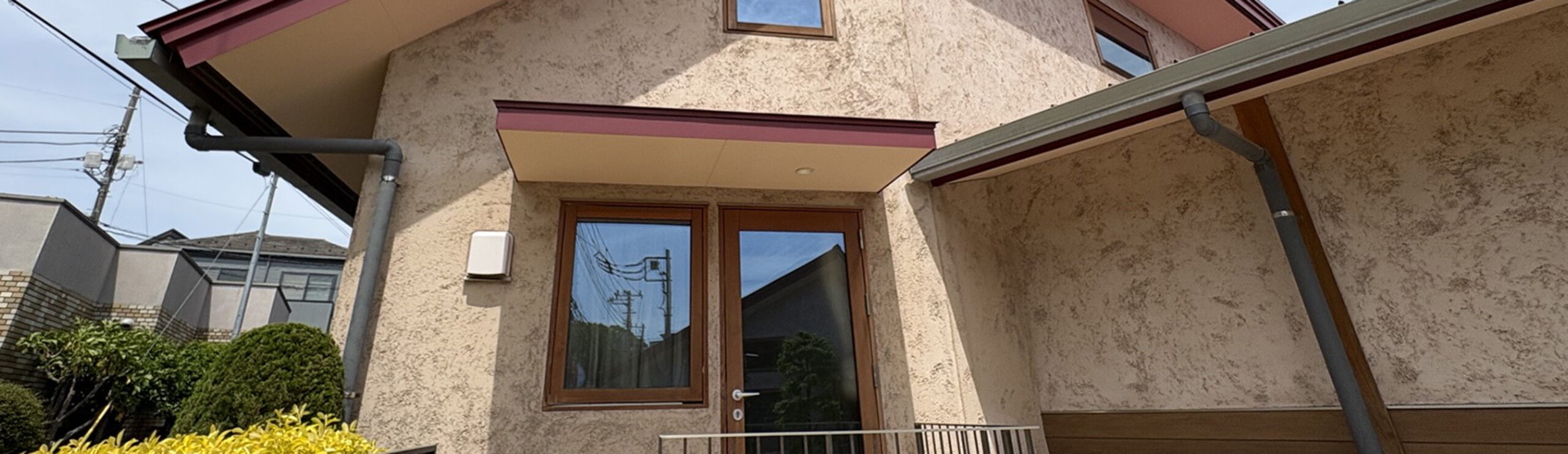 ベージュ色の壁と赤茶色の屋根が特徴的な施設の外観。正面に木枠のガラス扉の入り口がある。