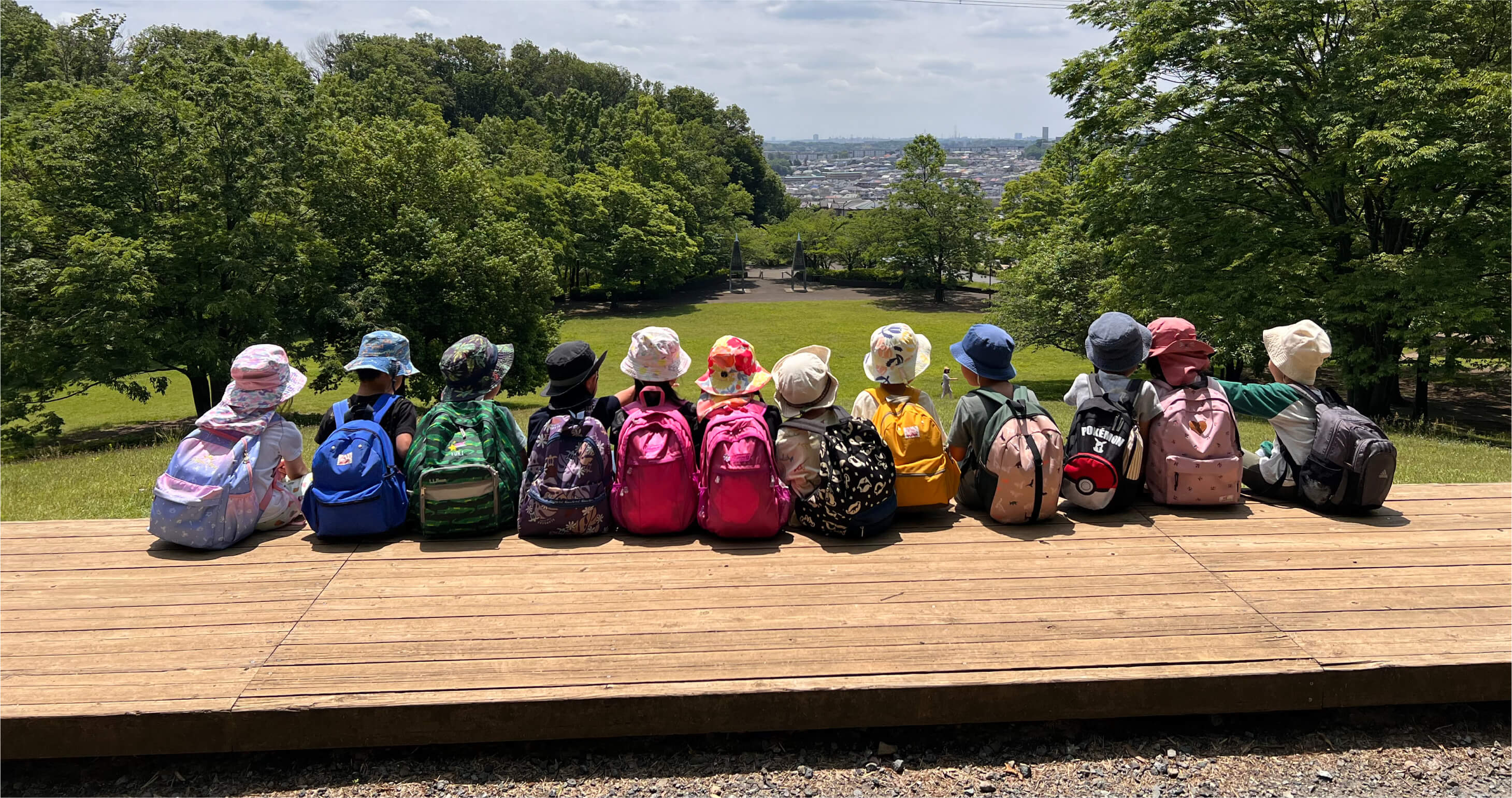 原っぱに座って、自然豊かな風景や街並みを眺める子どもたち