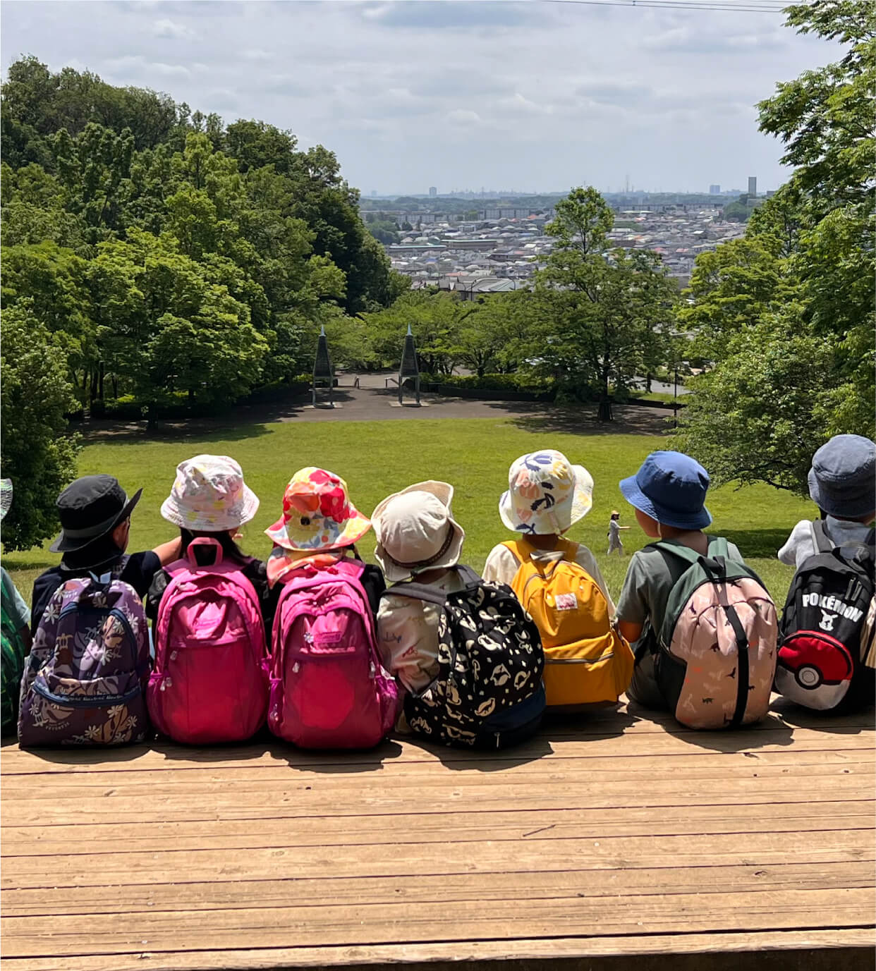 原っぱに座って、自然豊かな風景や街並みを眺める子どもたち